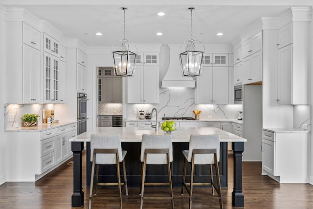 kitchen with white cabinets, a kitchen bar, backsplash, custom exhaust hood, and a center island with sink