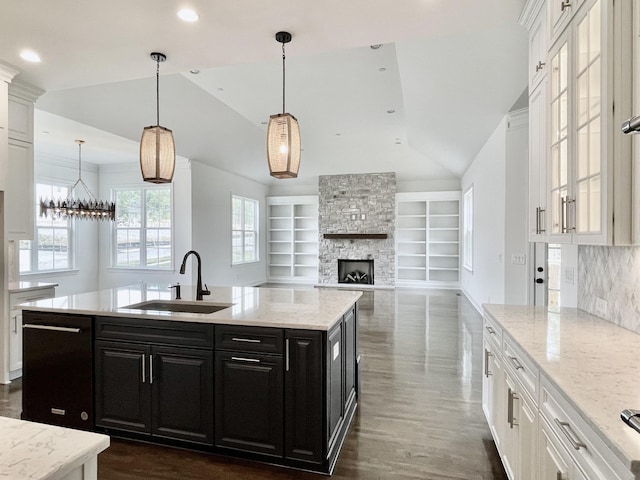 kitchen featuring pendant lighting, sink, built in features, black dishwasher, and a center island with sink