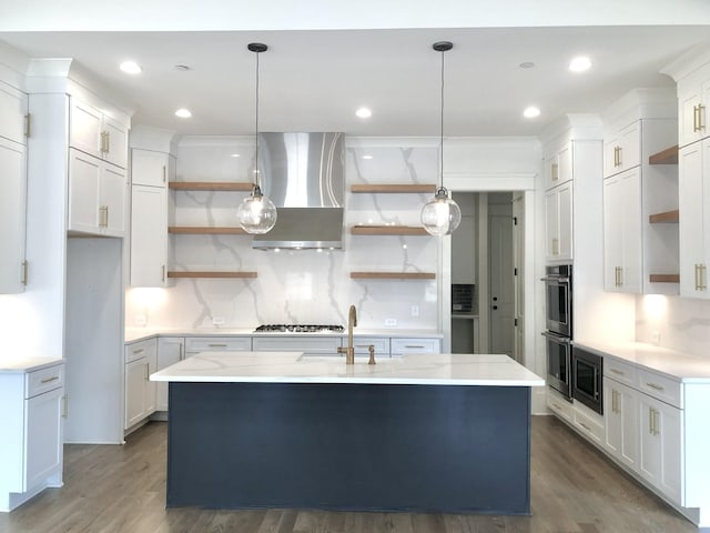 kitchen featuring hanging light fixtures, extractor fan, a center island with sink, and white cabinetry