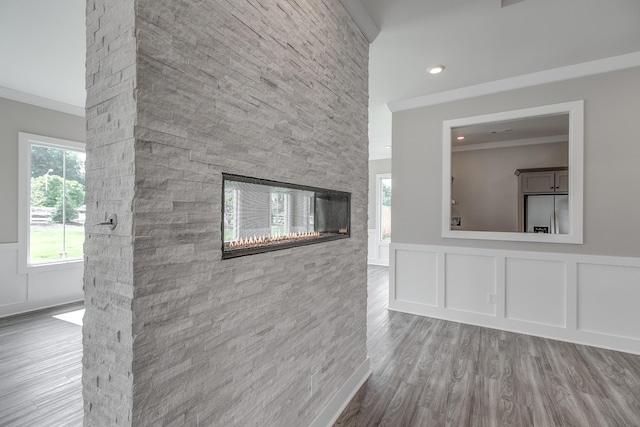 unfurnished living room featuring hardwood / wood-style floors, crown molding, and a stone fireplace