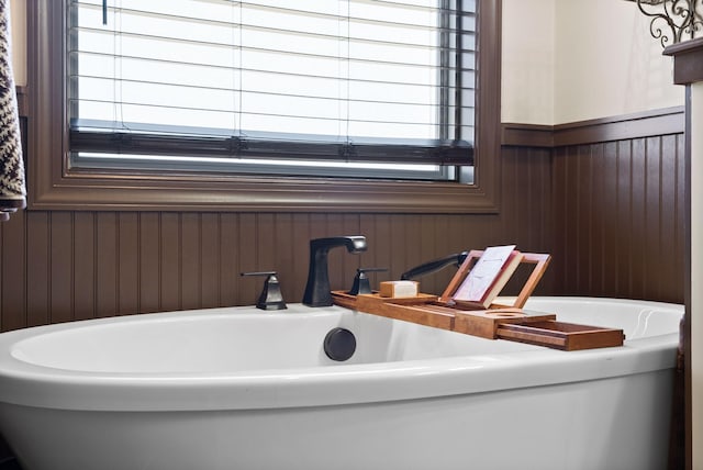 bathroom featuring a tub, sink, wood walls, and plenty of natural light