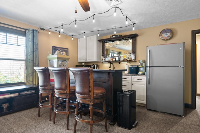 kitchen featuring a wealth of natural light, a kitchen breakfast bar, stainless steel refrigerator, and white cabinets