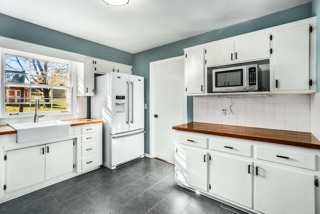 kitchen featuring white refrigerator with ice dispenser, sink, and white cabinets