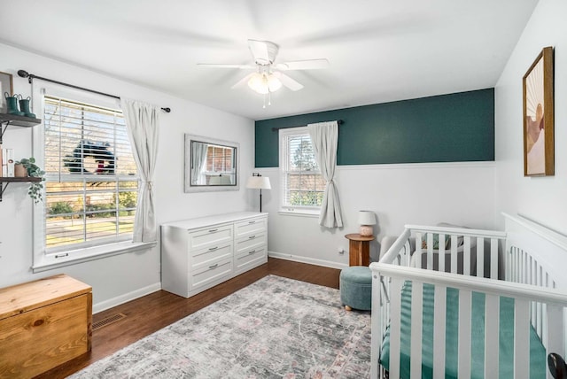 bedroom with dark hardwood / wood-style floors, a nursery area, and ceiling fan