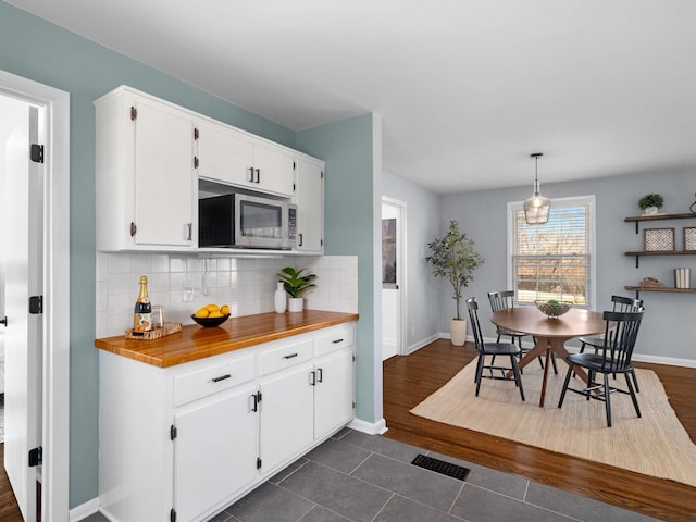 kitchen featuring decorative backsplash, stainless steel microwave, and white cabinetry