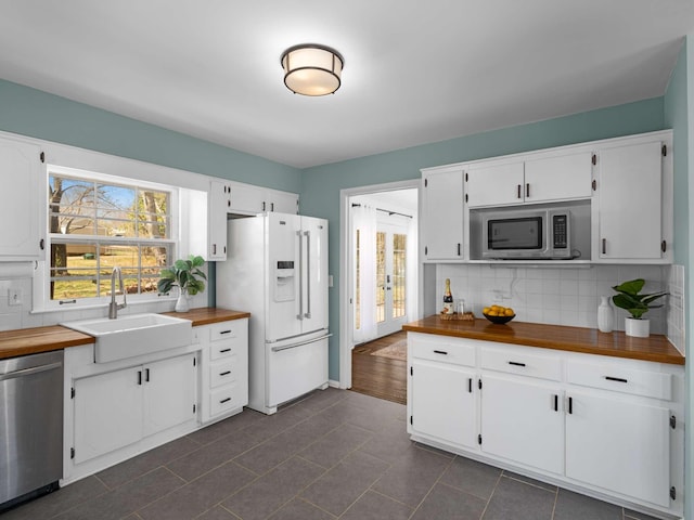 kitchen featuring a sink, white cabinetry, appliances with stainless steel finishes, decorative backsplash, and wooden counters