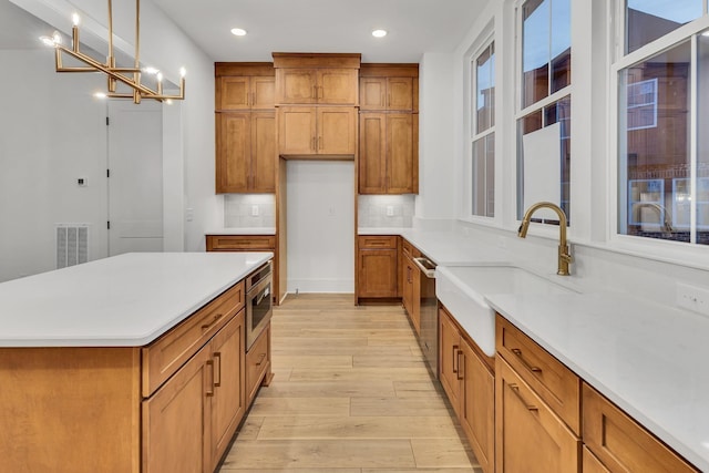 kitchen with decorative light fixtures, sink, backsplash, stainless steel appliances, and light hardwood / wood-style flooring