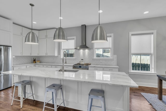 kitchen featuring white cabinetry, sink, wall chimney exhaust hood, and a center island with sink