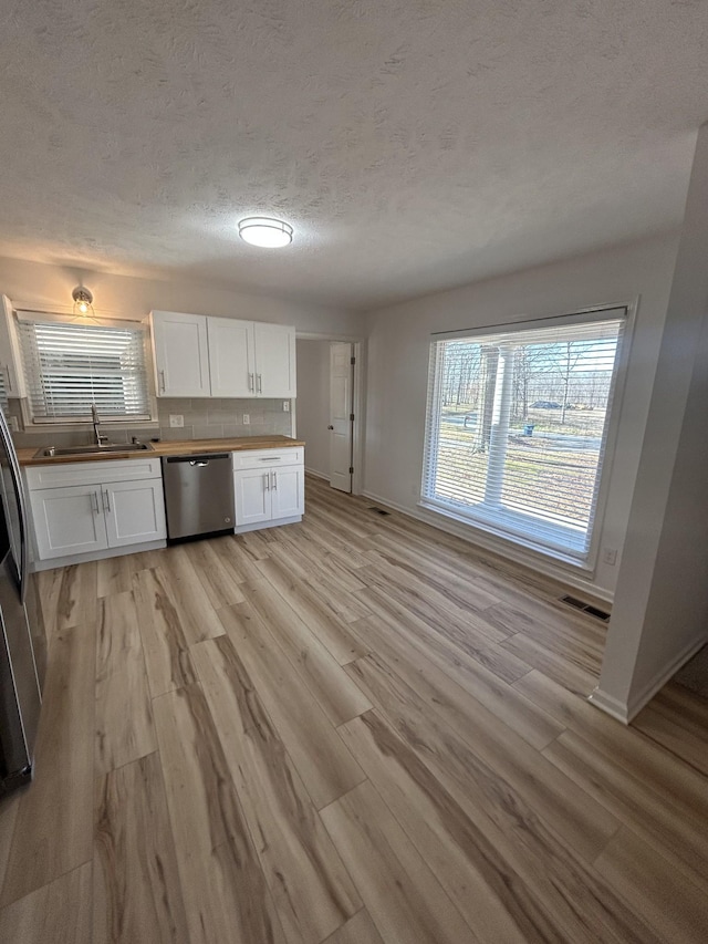 kitchen with appliances with stainless steel finishes, sink, light wood-type flooring, white cabinets, and a textured ceiling