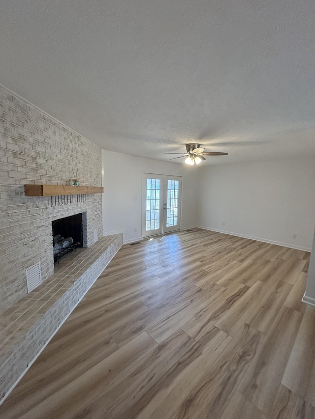 unfurnished living room with a brick fireplace, a textured ceiling, light wood-type flooring, and french doors