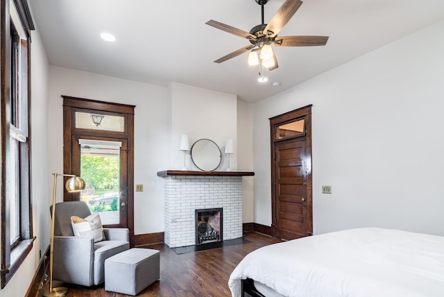 bedroom with dark wood-type flooring, ceiling fan, and a brick fireplace