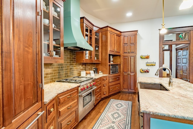 kitchen featuring sink, light stone counters, ventilation hood, hanging light fixtures, and appliances with stainless steel finishes