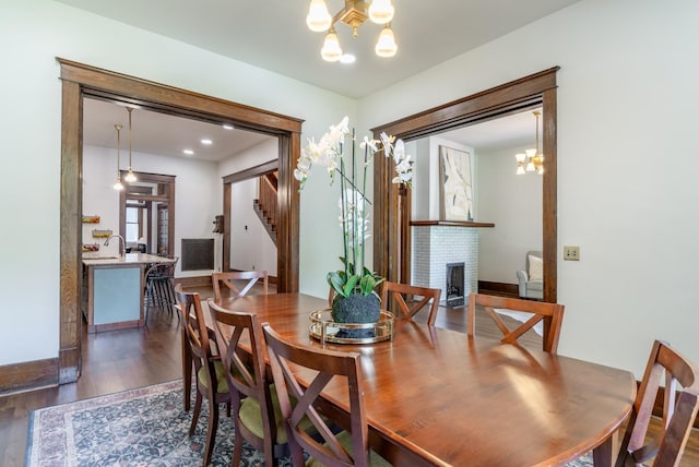 dining space featuring an inviting chandelier, a brick fireplace, and dark hardwood / wood-style flooring