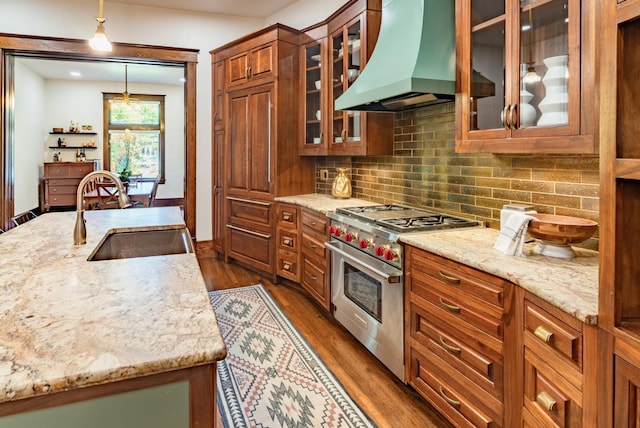 kitchen featuring sink, stainless steel stove, hanging light fixtures, light stone counters, and extractor fan