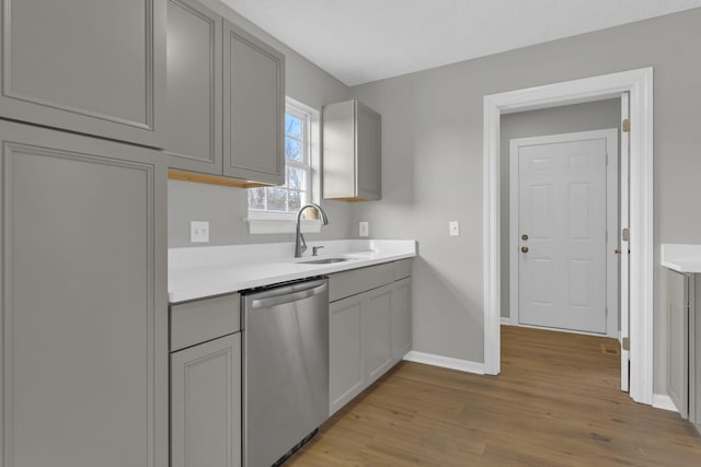 kitchen with gray cabinets, sink, stainless steel dishwasher, and light wood-type flooring