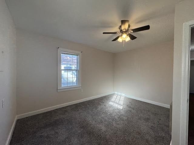 unfurnished room with ceiling fan and dark carpet