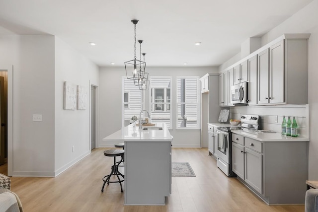 kitchen featuring appliances with stainless steel finishes, gray cabinets, an island with sink, and a breakfast bar area