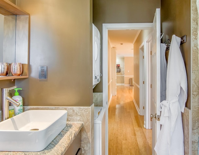 bathroom with stacked washer and dryer, ornamental molding, sink, and wood-type flooring