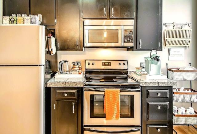 kitchen with stainless steel appliances, dark brown cabinets, and hardwood / wood-style floors