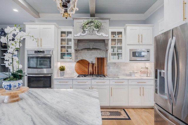 kitchen with appliances with stainless steel finishes, backsplash, light stone countertops, white cabinets, and beamed ceiling