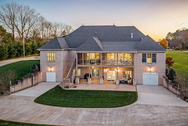 back house at dusk with a garage, a patio, and a yard