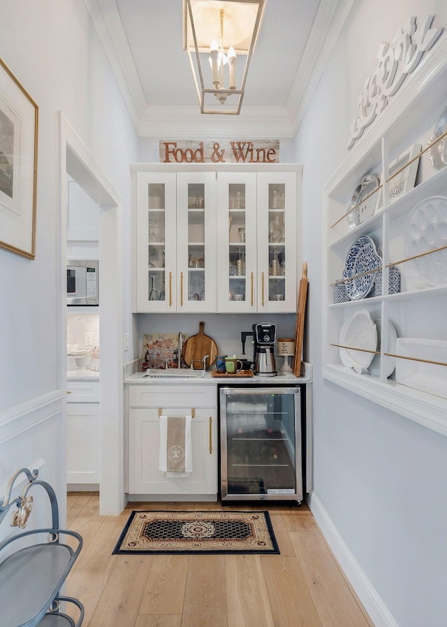 bar with white cabinets, sink, beverage cooler, and light hardwood / wood-style flooring