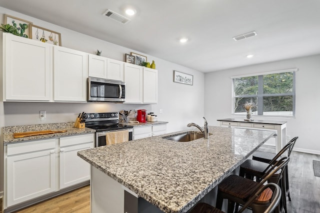 kitchen with sink, stainless steel appliances, an island with sink, and white cabinets