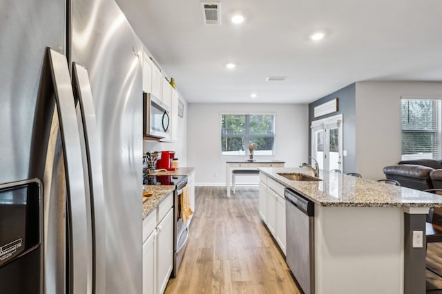 kitchen featuring stainless steel appliances, a center island with sink, white cabinets, and light stone counters