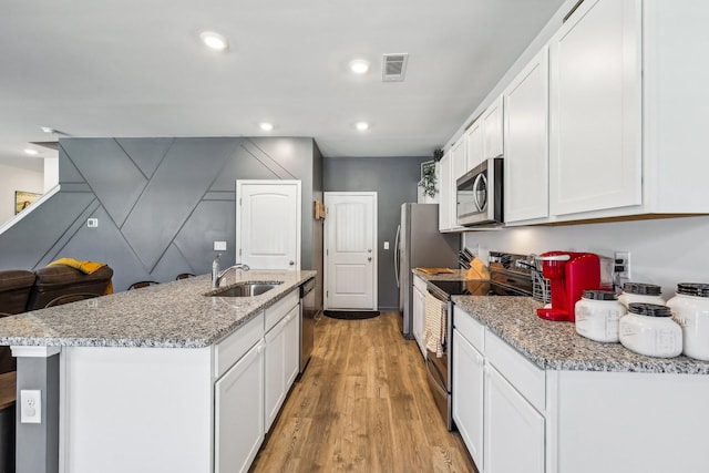 kitchen with sink, white cabinetry, light wood-type flooring, appliances with stainless steel finishes, and light stone countertops