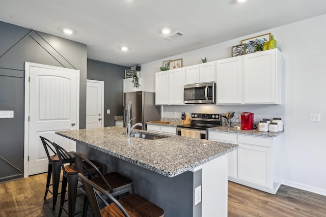 kitchen with stainless steel appliances, light stone countertops, sink, and a center island with sink