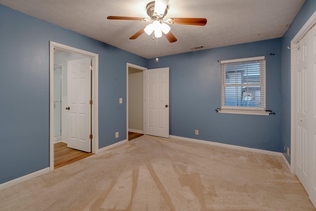 unfurnished bedroom with a closet, ceiling fan, light colored carpet, and a textured ceiling