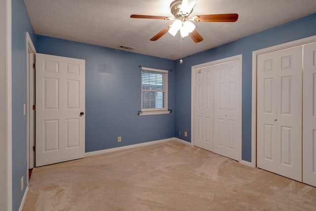 unfurnished bedroom featuring two closets, light colored carpet, a textured ceiling, and ceiling fan