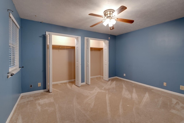 unfurnished bedroom featuring multiple closets, ceiling fan, light colored carpet, and a textured ceiling