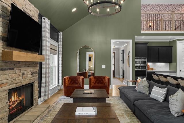 living room featuring a stone fireplace, light hardwood / wood-style flooring, high vaulted ceiling, and a chandelier