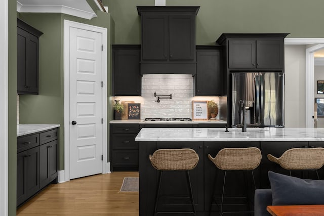 kitchen featuring sink, crown molding, light stone counters, gas cooktop, and stainless steel fridge