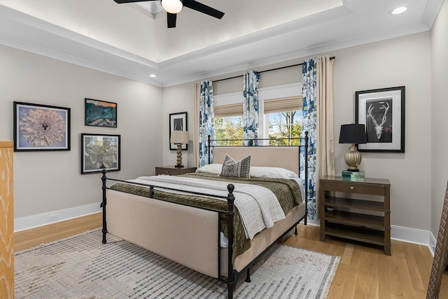 bedroom with light hardwood / wood-style flooring, a raised ceiling, and ceiling fan