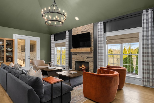 living room featuring light wood-type flooring, a notable chandelier, a fireplace, and french doors