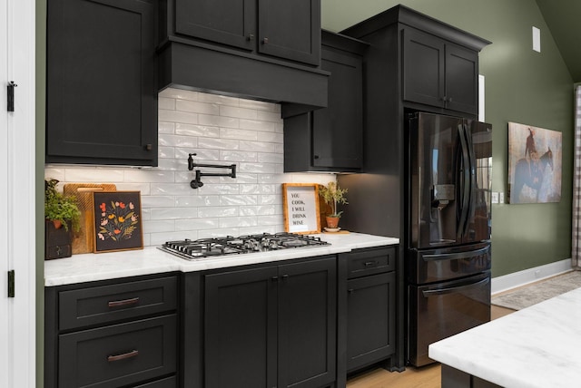 kitchen with vaulted ceiling, backsplash, light hardwood / wood-style floors, black refrigerator with ice dispenser, and stainless steel gas stovetop