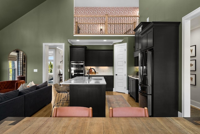 kitchen featuring sink, a kitchen island with sink, high vaulted ceiling, stainless steel appliances, and decorative backsplash