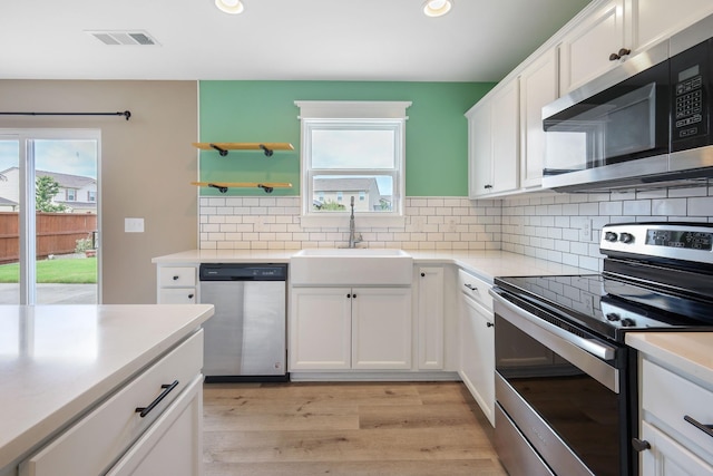 kitchen with appliances with stainless steel finishes, sink, white cabinets, and light hardwood / wood-style flooring