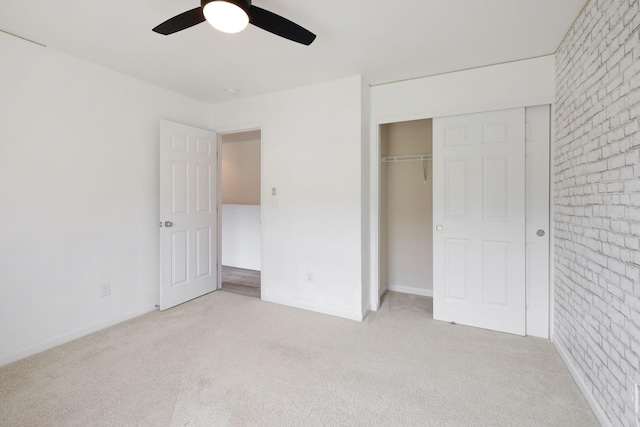 unfurnished bedroom featuring brick wall, light carpet, ceiling fan, and a closet