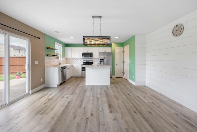 kitchen featuring appliances with stainless steel finishes, hanging light fixtures, a center island, light hardwood / wood-style floors, and white cabinets