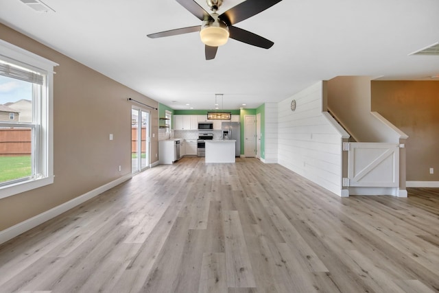 unfurnished living room featuring wooden walls, ceiling fan, and light hardwood / wood-style flooring