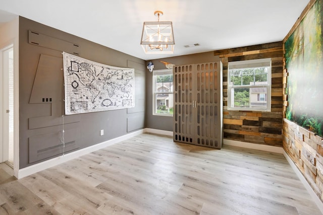 empty room with plenty of natural light, light hardwood / wood-style floors, a chandelier, and wood walls