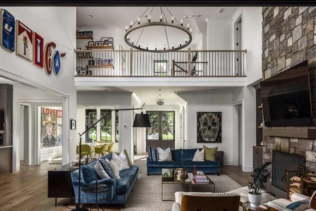 living room with a towering ceiling, an inviting chandelier, a fireplace, and wood finished floors