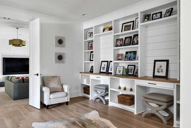 living area featuring baseboards, wood finished floors, built in features, and crown molding