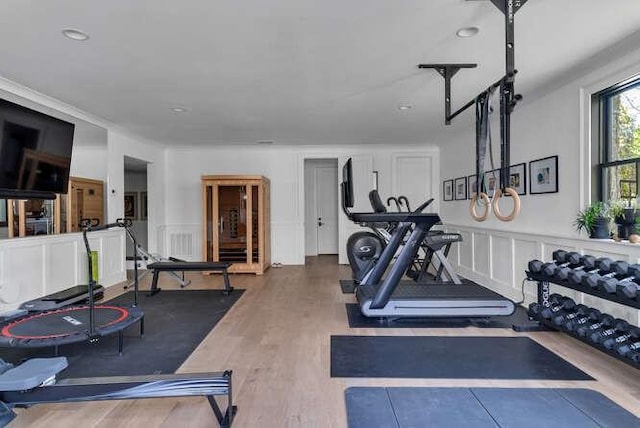 exercise area featuring a decorative wall, wood finished floors, and wainscoting