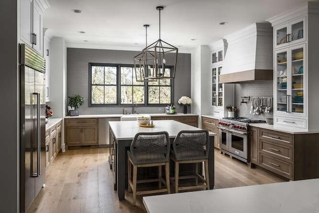 kitchen featuring high quality appliances, light countertops, a center island, glass insert cabinets, and custom range hood