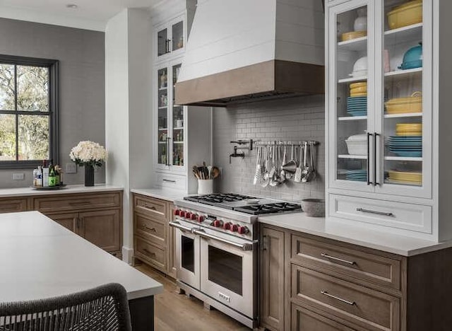 kitchen featuring light countertops, range with two ovens, brown cabinetry, and custom range hood