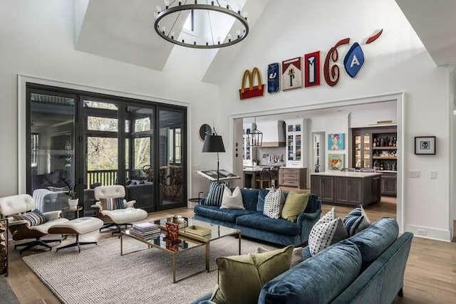 living room featuring a chandelier, light wood-type flooring, a towering ceiling, and baseboards